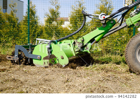 The tractor is cultivating the soil in the farm field. Freeing milling earth ground from old crops. The tractor is cultivating the soil in the farm field. Freeing milling earth ground from old crops. 94142282