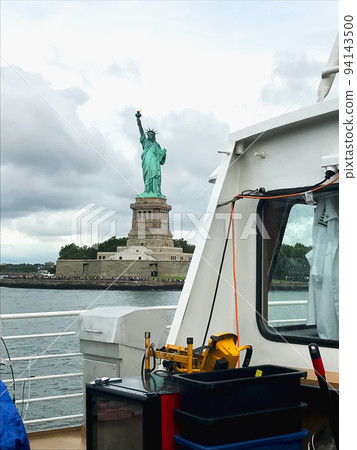 The Statue of Liberty on Liberty Island seen from a New York ferry under thick clouds on an overcast day 94143500