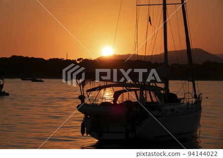 A white sailboat sails on the sea with an orange sunset 94144022
