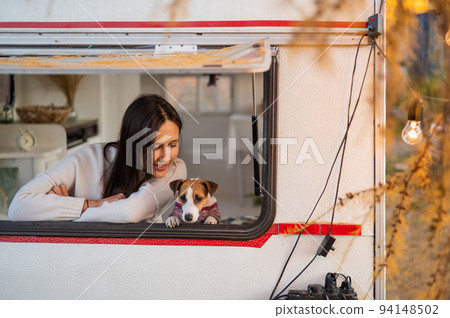 Caucasian woman looks out of the window of the van while hugging her dog Jack Russell Terrier. Travel in a camper in autumn. Caucasian woman looks out of the window of the van while hugging her dog Jack Russell Terrier. Travel in a camper in autumn. 94148502