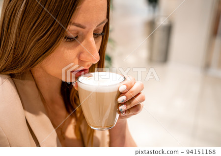 Close-up of beautiful female hands holding a large white cup of cappuccino. A woman is sitting in a cafe. Close-up of beautiful female hands holding a large white cup of cappuccino. A woman is sitting in a cafe. 94151168