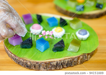 Thai Chef's hand is decorating Varieties traditional colorful Thai desserts set; steaming flour, black custard, coconut custard & steaming bean, layer pudding cake 94151889