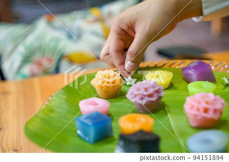 Thai Chef's hand is decorating Varieties traditional colorful Thai desserts set; steaming flour, black custard, coconut custard & steaming bean, layer pudding cake 94151894