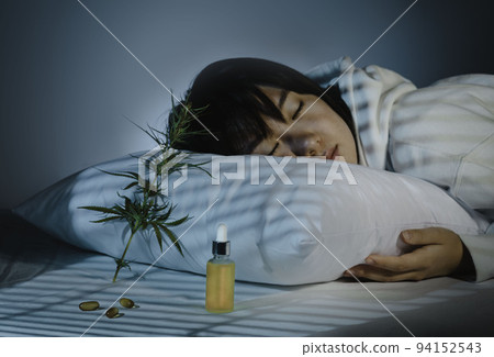 Asian girl sleeping in evening bedroom with cbd oil, capsules and a cannabis branch. Melatonin production, concept of combat sleep disorders 94152543