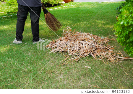 Worker sweeps dry leafs in garden. Worker sweeps dry leafs in garden. 94153183