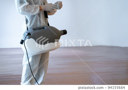 Professional technical man in prevention suit sprays sterilizing solution.by electrical prepares himself before spray machine on the wood floor and white background with studio light. 94155684