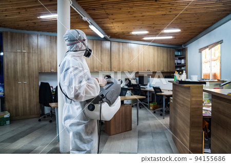 Professional technical man in prevention suit with his sterilizing machine and disinfecting water sprays all areas in the office room to take purifying coronavirus (COVID-19). Professional technical man in prevention suit with his sterilizing machine and disinfecting water sprays all areas in the office room to take purifying coronavirus (COVID-19). 94155686