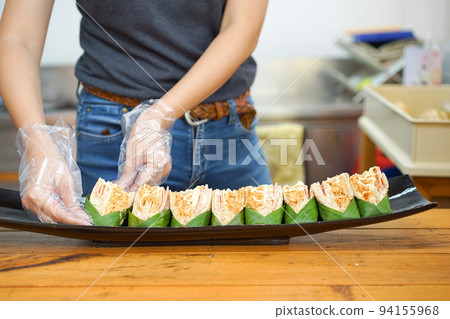 Dried shredded pork sandwiches are arranged on the black boat dish shape by an Asian young woman wears plastic gloves. 94155968