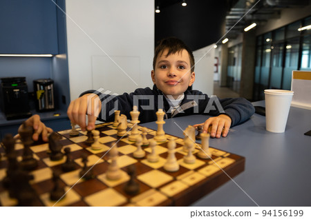 Smart Caucasian boy holding a chess piece and moving it on a chessboard during chess strategy lesson. Intelectual hobby Smart Caucasian boy holding a chess piece and moving it on a chessboard during chess strategy lesson. Intelectual hobby 94156199