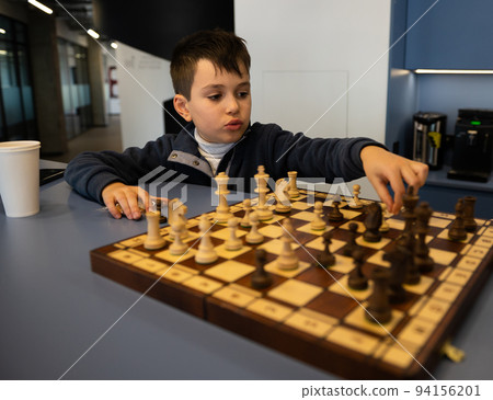 Adorable smart elementary age boy thinking on chess move, developing strategy while playing chess. Intelligent hobby 94156201