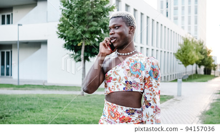 Black gay person in feminine clothes speaking on smartphone 94157036