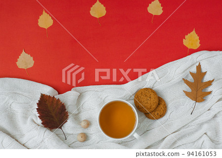 Autumn flat lay composition. A cup of tea, a knitted blanket, autumn dry leaves, oatmeal cookies on a red background top view. The concept of falling Autumn flat lay composition. A cup of tea, a knitted blanket, autumn dry leaves, oatmeal cookies on a red background top view. The concept of falling 94161053