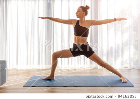 Young lady in black sportswear doing yoga in the room with big window Young lady in black sportswear doing yoga in the room with big window 94162855