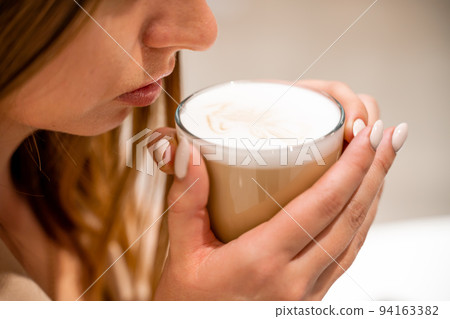 Close-up of beautiful female hands holding a large white cup of cappuccino. A woman is sitting in a cafe. Close-up of beautiful female hands holding a large white cup of cappuccino. A woman is sitting in a cafe. 94163382