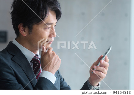 A middle-class businessman in a suit who operates a smartphone in the office 94164518