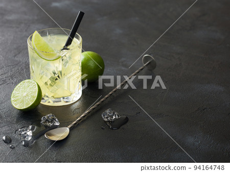 Gimlet Kamikaze cocktail in crystal glass with lime slice and ice on black board with fresh limes and spoon. 94164748
