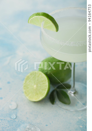 Crystal glass of Margarita cocktail with fresh limes on light blue table background Crystal glass of Margarita cocktail with fresh limes on light blue table background 94164753