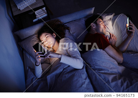 Couple using smartphones in bed before sleep Couple using smartphones in bed before sleep 94165173