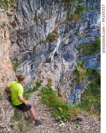 Boy at top of path with steel chain anchored in the rocky wall Boy at top of path with steel chain anchored in the rocky wall 94165357