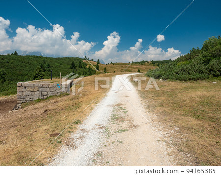 Gravel road to hill peak. Dusty mountain road in Dolomite Alps. 94165385