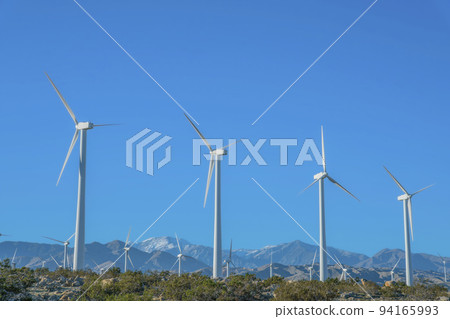 Windmills with three sharp blades against mountains and blue sky background Windmills with three sharp blades against mountains and blue sky background 94165993