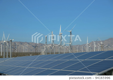 Windmills and solar panels against mountain and blue sky background Windmills and solar panels against mountain and blue sky background 94165996