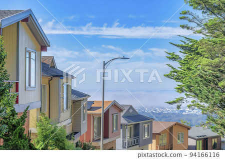 Row of houses on a sunlit street against blue sky and clouds on a sunny day 94166116
