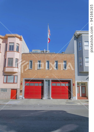 Front view of a building with red garage doors and flag against clear blue sky Front view of a building with red garage doors and flag against clear blue sky 94166165