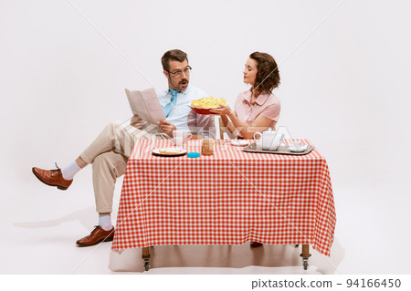 Portrait of loving couple sitting at the table, having breakfast isolated on white background. Wife giving apple pie Portrait of loving couple sitting at the table, having breakfast isolated on white background. Wife giving apple pie 94166450