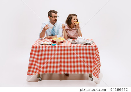 Portrait of beautiful couple sitting at the table, having breakfast isolated on white background. Husband looking at wife with love Portrait of beautiful couple sitting at the table, having breakfast isolated on white background. Husband looking at wife with love 94166452