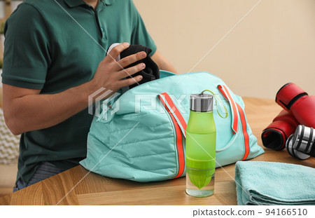 Man packing sports bag for training indoors, closeup Man packing sports bag for training indoors, closeup 94166510
