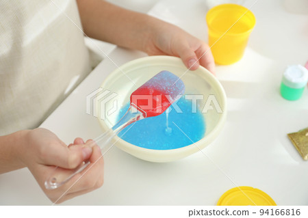 Little girl mixing ingredients with silicone spatula at table, closeup. DIY slime toy 94166816