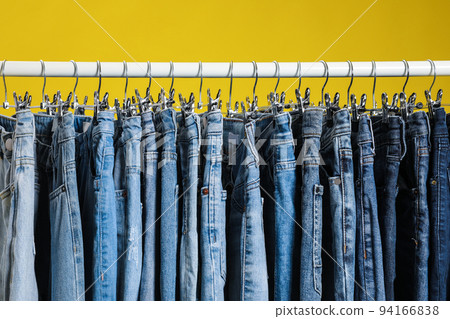 Rack with different jeans on yellow background Rack with different jeans on yellow background 94166838