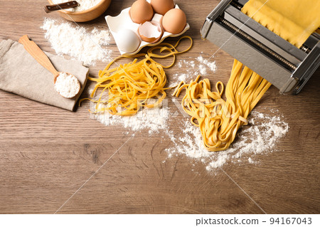 Pasta maker machine with dough and products on wooden table, above view. Space for text Pasta maker machine with dough and products on wooden table, above view. Space for text 94167043