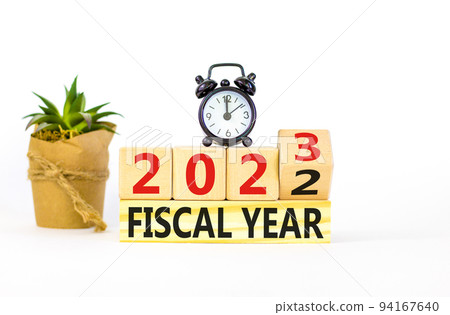 2023 fiscal year symbol. Wooden cubes with words 2022 Fiscal year to 2023 Fiscal year. Beautiful white table white background. Black alarm clock. Business and 2023 fiscal year concept. Copy space. 94167640