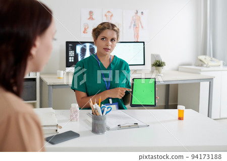 Medical nurse talking to patient and pointing at green chroma key tablet screen with VFX motion tracking markers 94173188