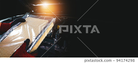 New air filter in plastic wrap of a car holding by auto mechanic hand with engine compartment New air filter in plastic wrap of a car holding by auto mechanic hand with engine compartment 94174298