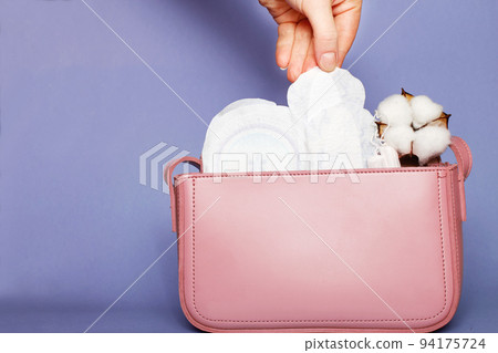Women's hand takes out panty liner from pink cosmetic bag with tampons and feminine sanitary pads Women's hand takes out panty liner from pink cosmetic bag with tampons and feminine sanitary pads 94175724