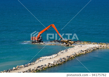 An excavator and a mining truck move stones into the sea. Construction of breakwaters to protect the beach in Netanya in Israel. An excavator and a mining truck move stones into the sea. Construction of breakwaters to protect the beach in Netanya in Israel. 94175762