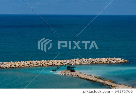 The excavator moves stones into the sea. Construction of breakwaters to protect the beach in Netanya in Israel. The excavator moves stones into the sea. Construction of breakwaters to protect the beach in Netanya in Israel. 94175766