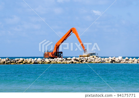 An excavator and a mining truck move stones into the sea. Construction of breakwaters to protect the beach in Netanya in Israel. 94175771