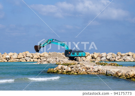 The excavator moves stones into the sea. Construction of breakwaters to protect the beach in Netanya in Israel. The excavator moves stones into the sea. Construction of breakwaters to protect the beach in Netanya in Israel. 94175773