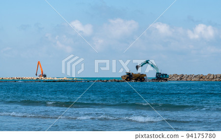 An excavator and a mining truck move stones into the sea. Construction of breakwaters to protect the beach in Netanya in Israel. 94175780