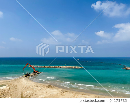 An excavator and a mining truck move stones into the sea. Construction of breakwaters to protect the beach in Netanya in Israel. 94175783