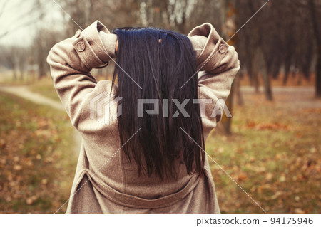 portrait of brunette hair woman in beige coat walking at the city park . 94175946