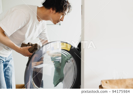 A man putting laundry into the washing machine A man putting laundry into the washing machine 94175984