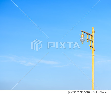 Beautiful design of golden post of public street lamp with blue sky and little white cloud as background. Complementary color. 94176270