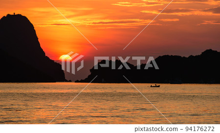 Half of beautiful sun and white cloud in the orange sky with silhouette fisherman on the long tail boat and islands in the sea as foreground. Warm tone. Rule of third composition. Half of beautiful sun and white cloud in the orange sky with silhouette fisherman on the long tail boat and islands in the sea as foreground. Warm tone. Rule of third composition. 94176272