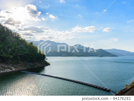 Beautiful view of the reservoir over Srinakarin dam located in Kanchanaburi province in the western of Thailand with beautiful blue sky, white cloud, golden sunlight and mountain as background. Beautiful view of the reservoir over Srinakarin dam located in Kanchanaburi province in the western of Thailand with beautiful blue sky, white cloud, golden sunlight and mountain as background. 94176281