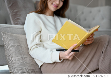 Asian female chilling in her living room, reading a book or playing a word scramble game 94176902